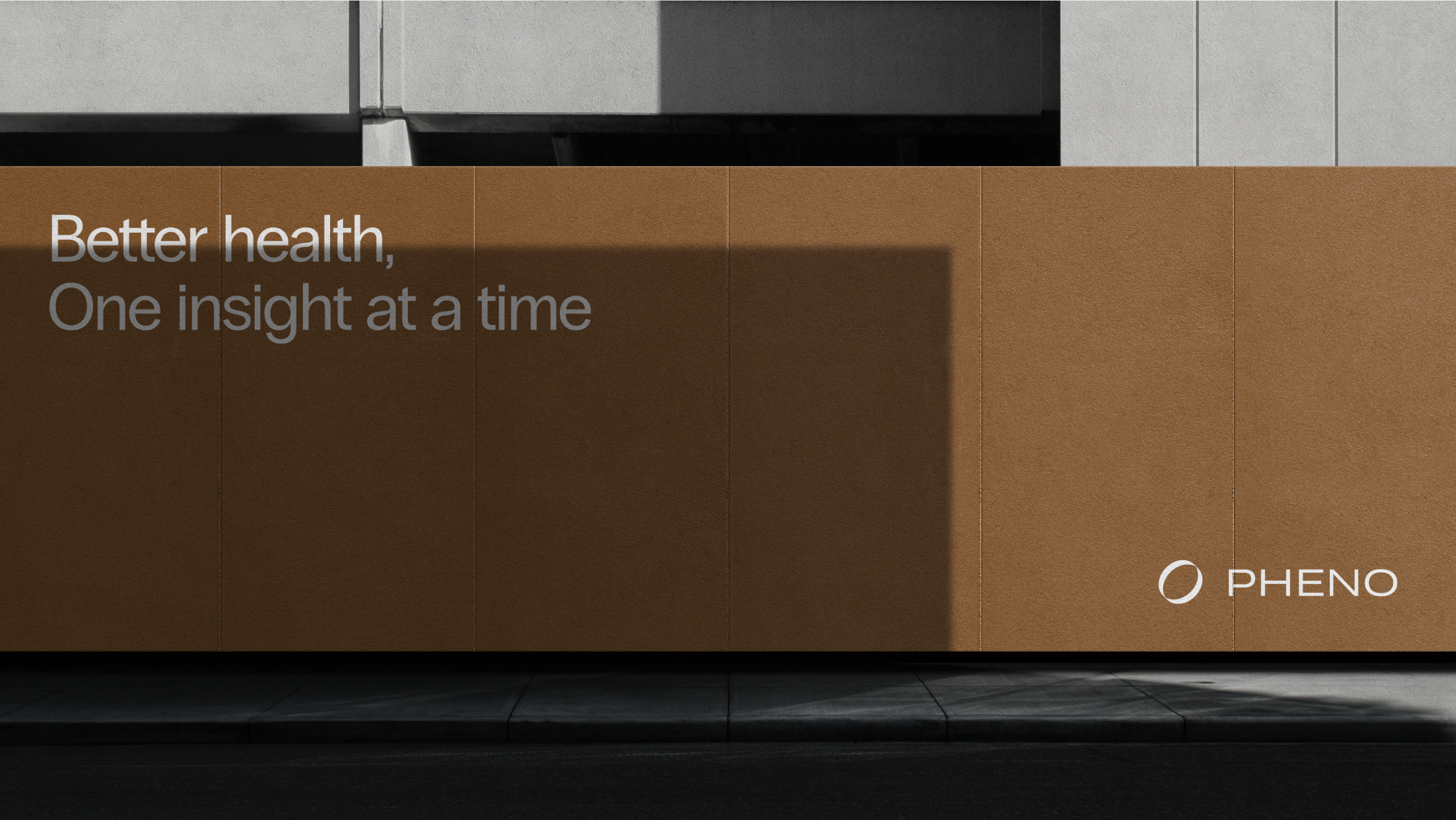 Pheno branding on brown wall with the text "Better health, One insight at a time" in urban setting.